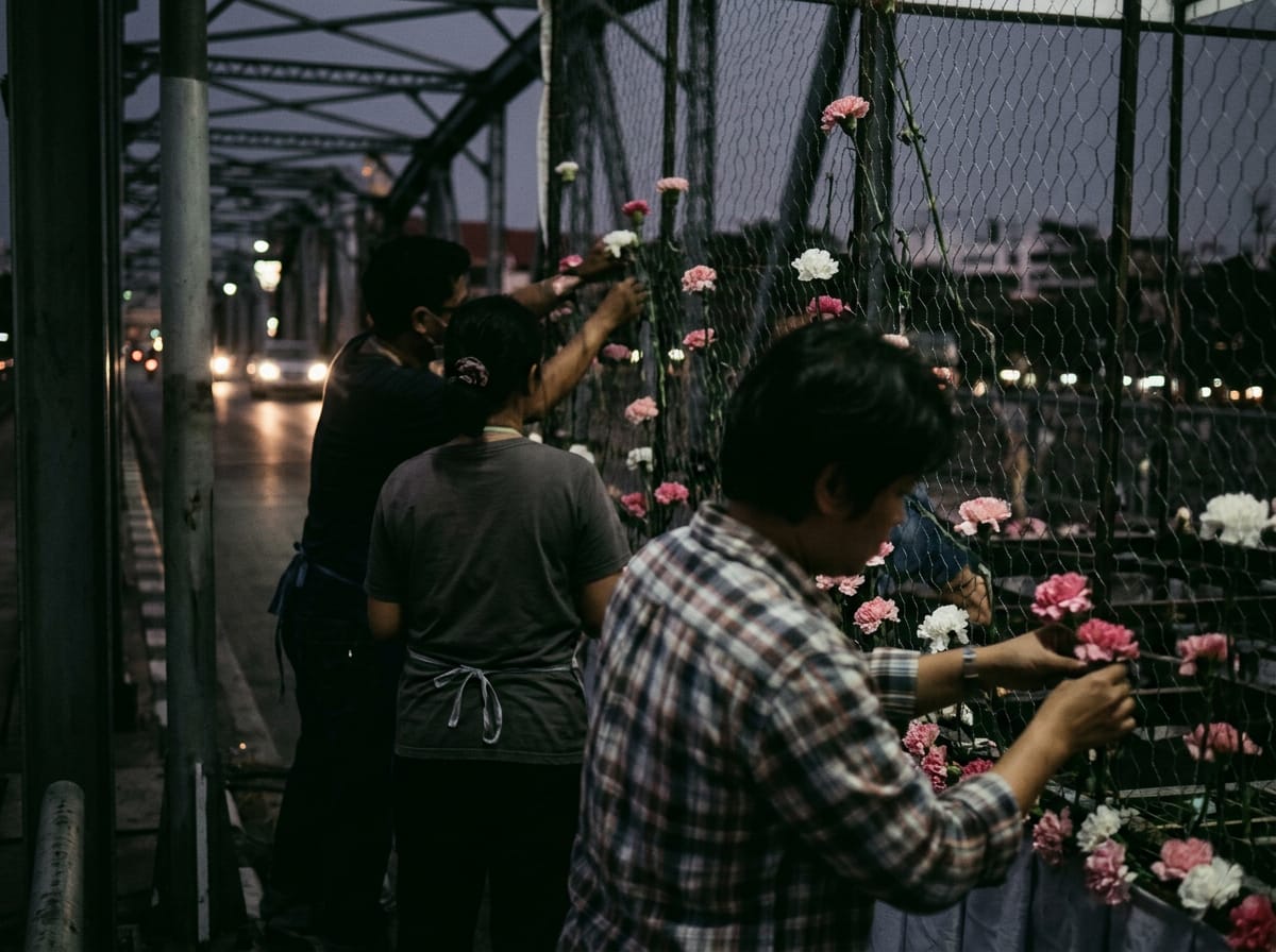 Volunteers pinning carnations onto a parade float frame at Nawarat Bridge before dawn