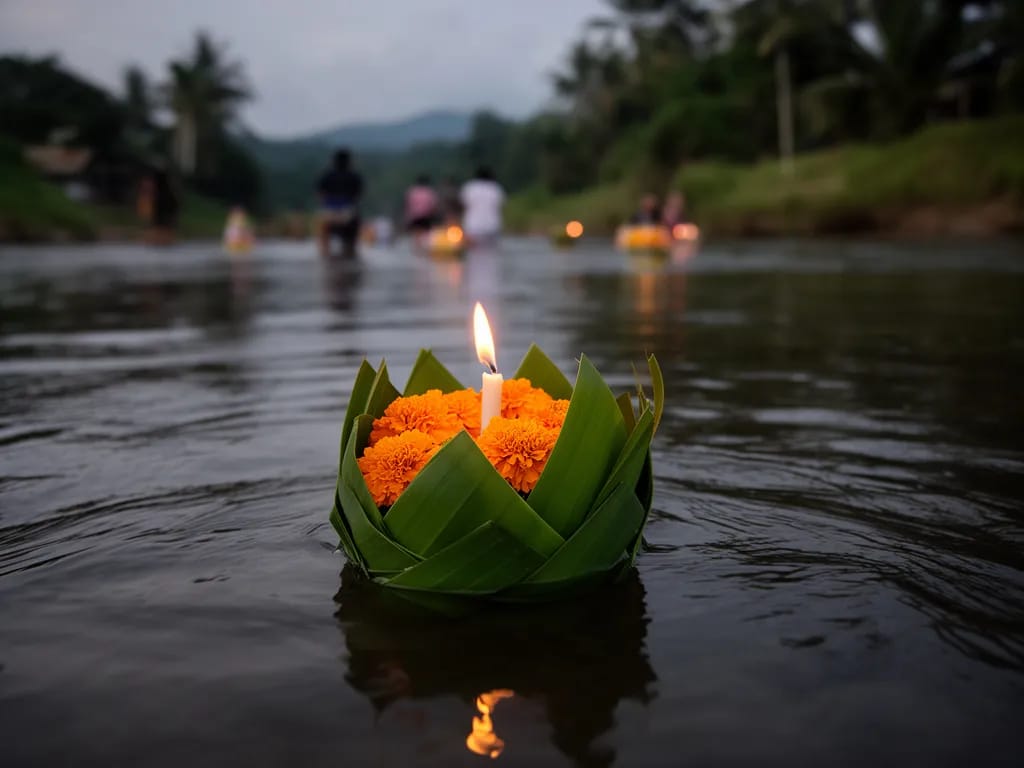 Banana-leaf krathong with marigolds and a candle floating on the dark Ping River