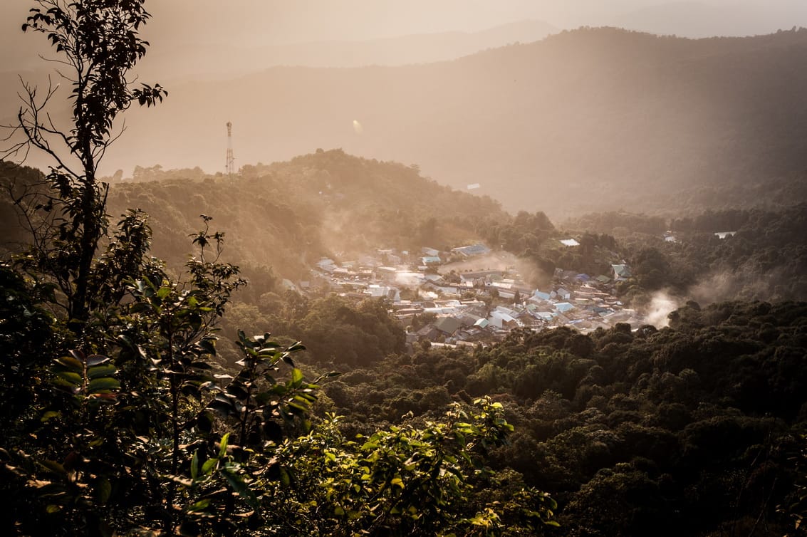 Hmong village of Doi Pui near the summit, seen from the forested ridge above in hazy afternoon light