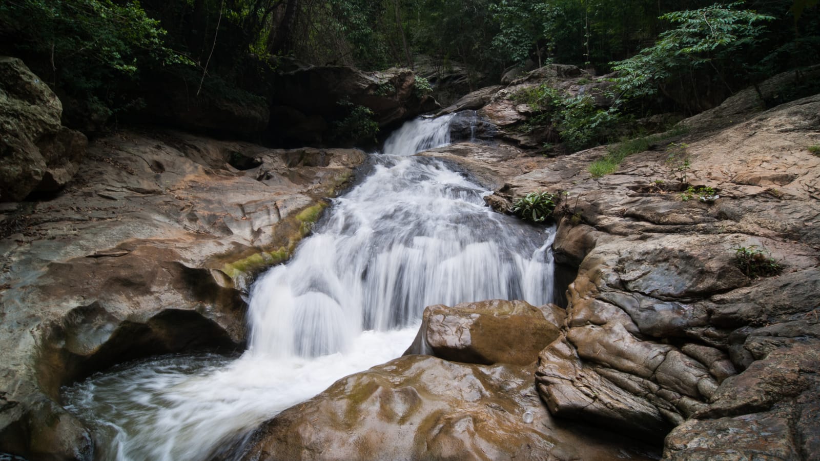 One of the tiers of Mae Sa waterfall cascading over smooth rocks into a pool