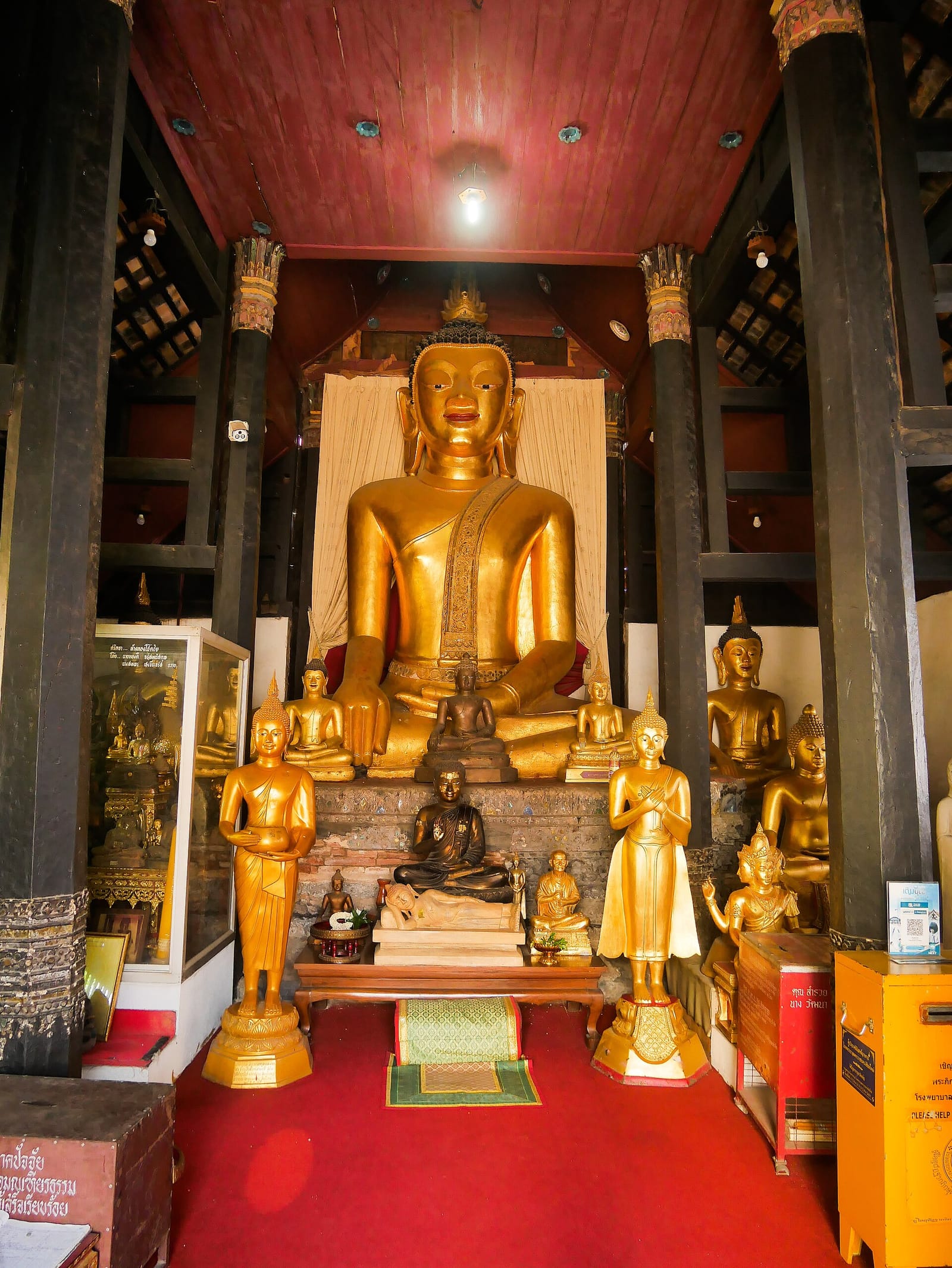 Principal Buddha image inside the teak viharn, in the maravijaya posture on a raised altar flanked by attendant Buddha images