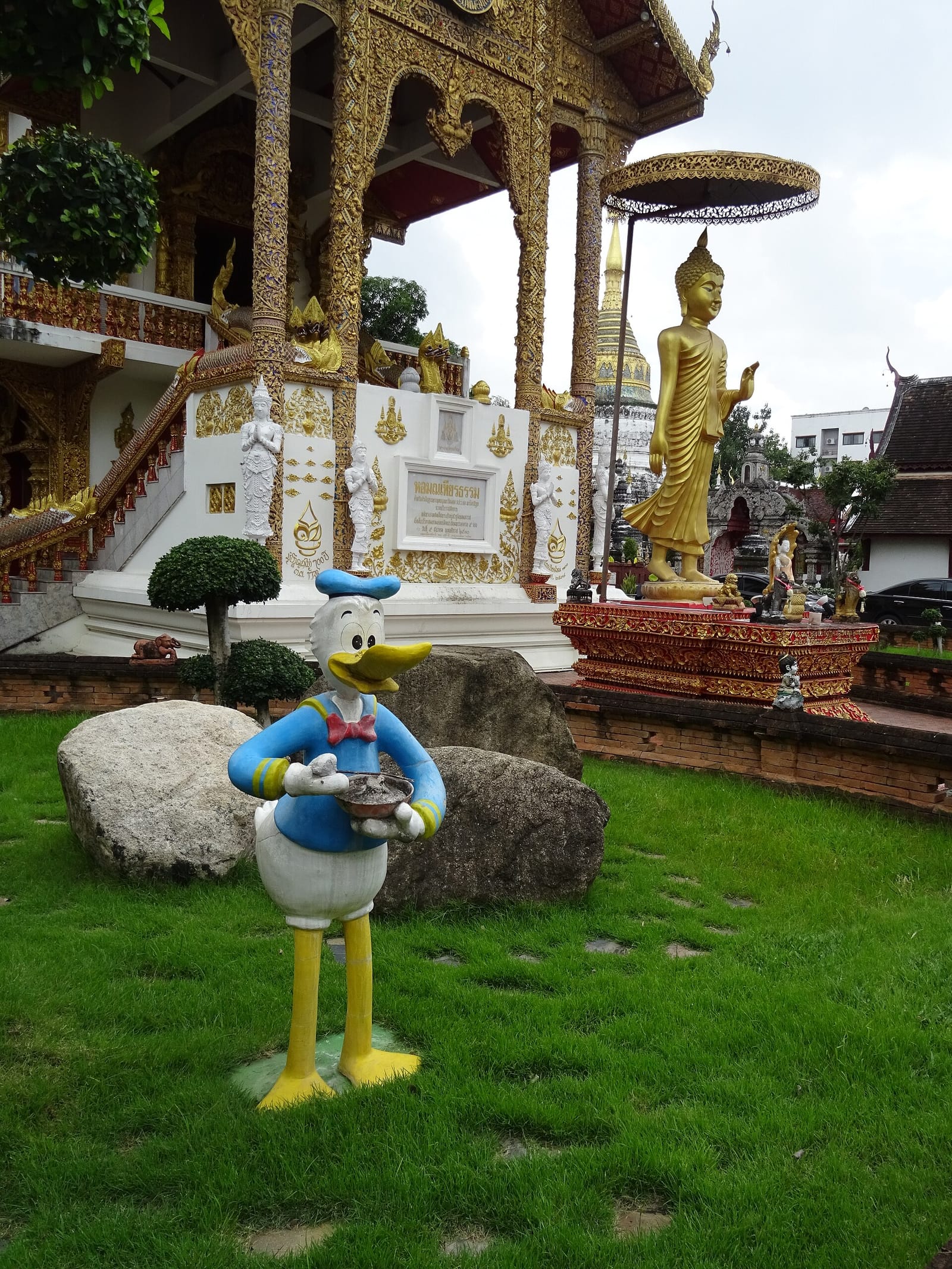 Painted concrete Donald Duck statue holding an alms bowl on the lawn in front of the modern hall