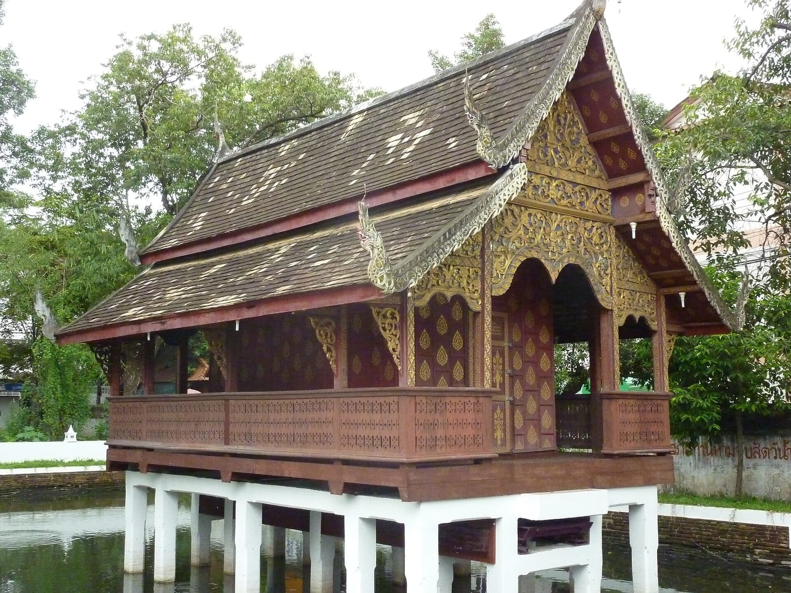 Teak ho trai scripture library raised on whitewashed pillars above its pond at the south of the compound