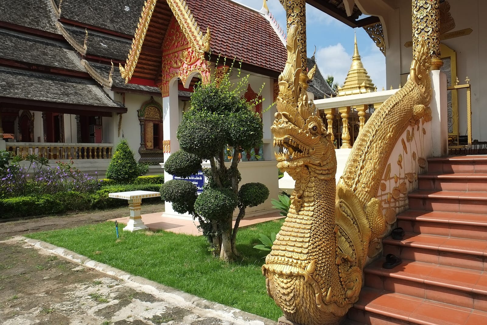 Gilded naga balustrade on an entrance staircase at Wat Chiang Man, with the gold spire of the chedi behind