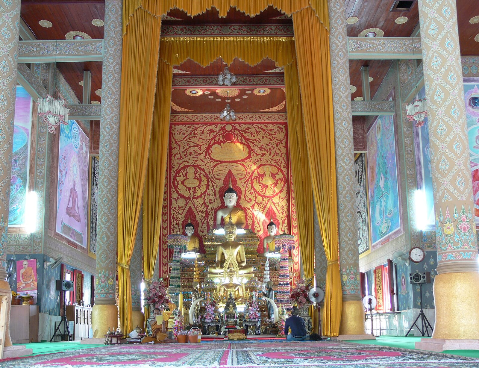 Principal gilded Buddha image on the altar inside the main viharn, flanked by smaller images and murals