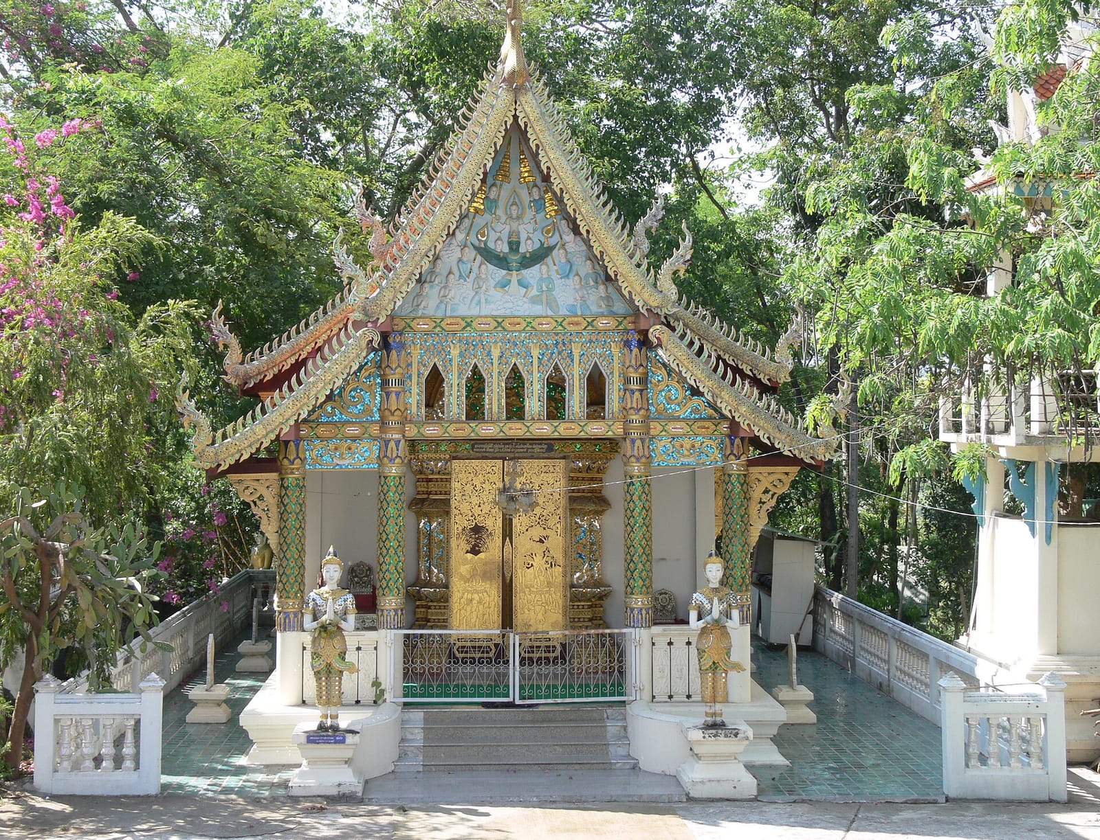 The small ubosot of Wat Doi Saket, flanked by paired guardian statues on the tree-shaded terrace