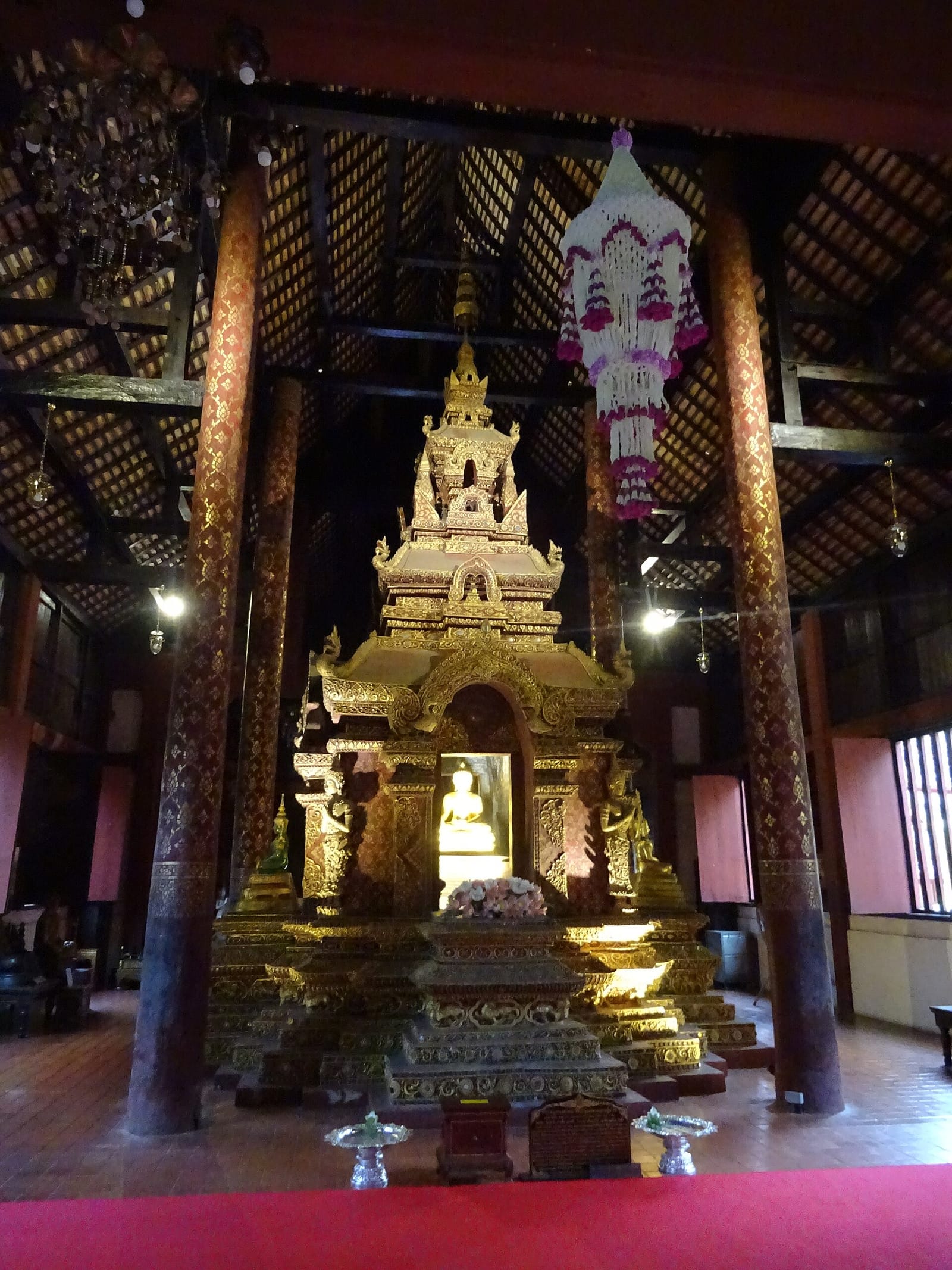 Interior of the ubosot showing the principal Buddha image inside its gilded shrine, flanked by lacquered pillars