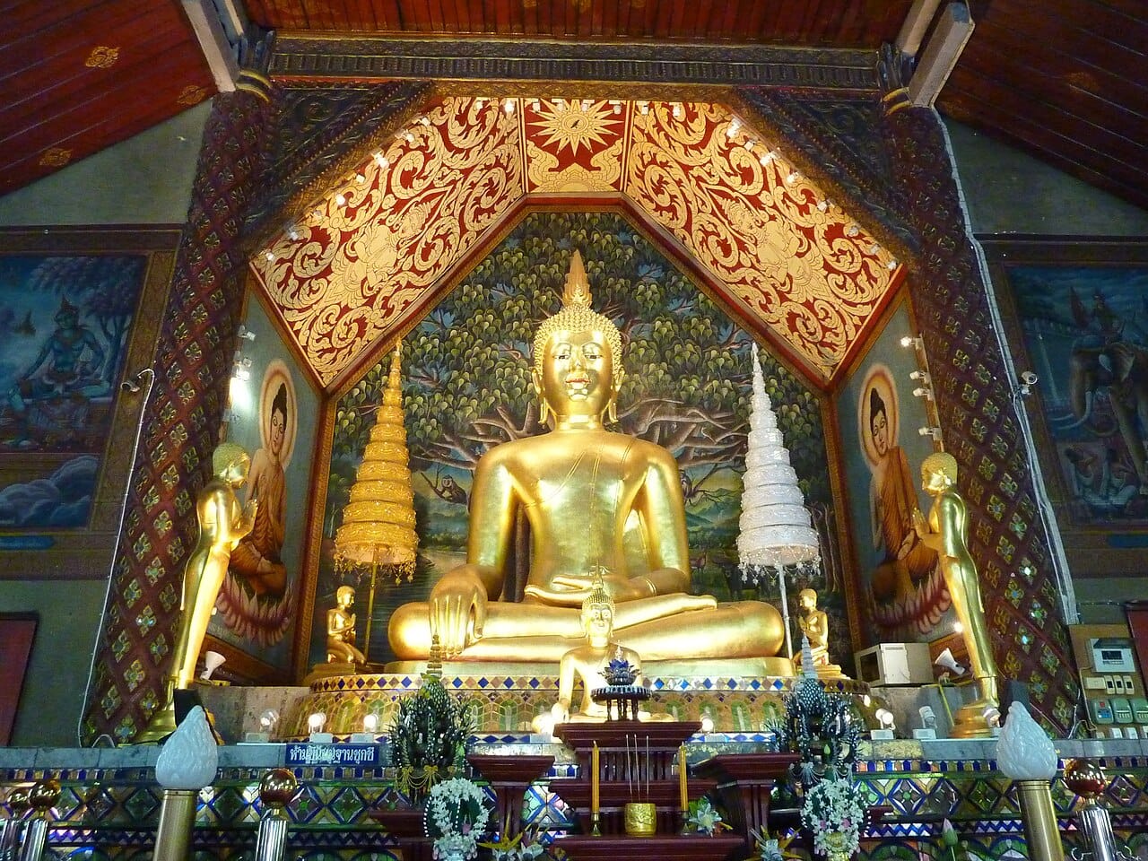 Seated Buddha image inside a shrine hall on the upper terrace, framed by gilded lai kham gable decoration