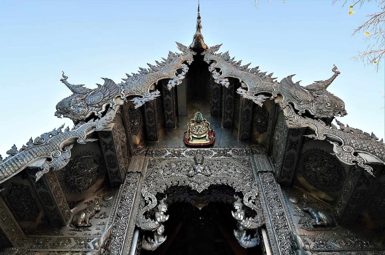 Embossed silver pediment and naga bargeboards of the silver ubosot seen from below, with Buddhist iconography in deep relief