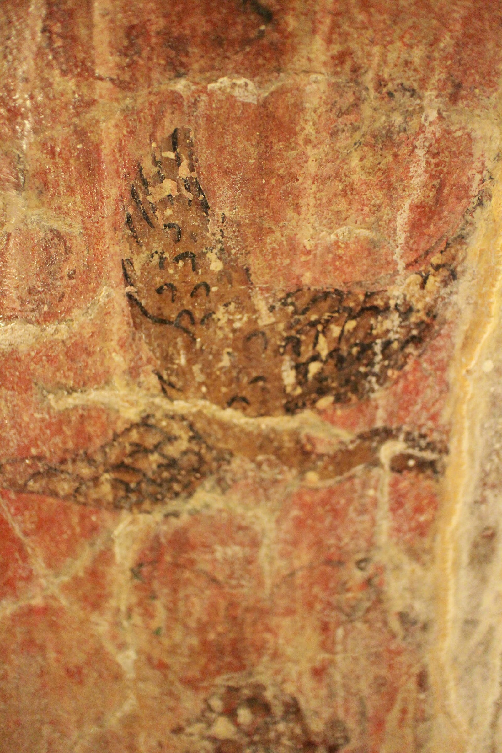 Faded ancient mural of a bird on the red ochre plaster of the tunnel walls at Wat Umong